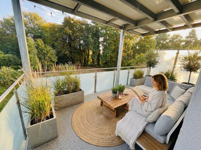 Visualisierung: überdachter Balkon mit Sofa, Pflanzkübeln und Blick in die Bäume